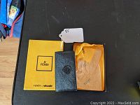 Top view of unopened black leather keychain holder placed on original yellow Fendi box with branded tissue paper inside the box.