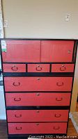 Full front view of antique Japanese cabinet showing red lacquered sliding doors and drawers with black framing, metal handles, and pulls.
