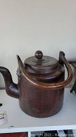 Front view of antique Japanese metal kettle with large curved spout and wooden handle raised above lid.