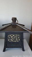 Front view of dark metal antique Japanese-style lantern with ornate cutouts and roof handle