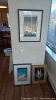 Three framed prints leaning against wall, one hung