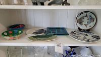 Shelf of decorative ceramic plates and bowls, including floral, abstract, fish designs, and various colors.