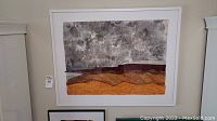 Full view of the framed mixed media art hung on wall showing abstract landscape with textured mountainous sections and cloudy sky.