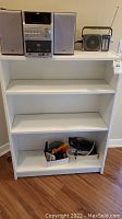 White IKEA shelving unit front view with some items on top and inside lower shelf.