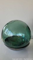 Front view of green Japanese glass fishing ball showing shape and reflective surface on copper bowl base