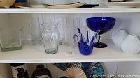 Shelf with various glassware including Murano art glass, Reijmyre bowl, clear glass vases, and white pottery vases.