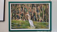 Framed artwork of white egret standing in water with wooded background.