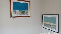 Overview of both framed artworks hanging on wall: wooden frame on left, gray frame on right
