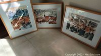 Three framed watercolors leaning against a wall on tile floor