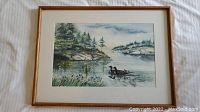 Framed watercolour painting showing swimming geese on a lake with landscape of trees and rocks.