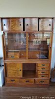 Front view of assembled two-piece cabinet showing upper wood doors, middle glass doors and lower drawer section
