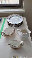 Photo of three Wedgwood dishes including creamer, sugar dish with missing lid and repairs, and small pitcher alongside stacked Tiffany & Co. plates.