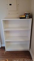 Front view of the white IKEA bookshelf showing three shelves and slight scratches.