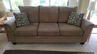 Front view of three seater Flair Design sofa with brown corduroy upholstery and two patterned throw pillows.