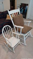 Two white wooden rocking chairs, one large with brown seat and back cushions, and one small child-sized without cushions.