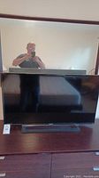 Front view of the Sony Bravia TV on a dark brown wooden surface with reflection of person taking photo