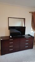 Front view of the chocolate brown dresser with eight drawers and a mirror above it. A TV sits on top, not included in the lot.