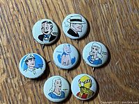 Top view of seven Kellogg's Pep cereal premiums featuring colorful character illustrations on the front of metal pins.
