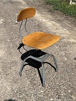 Photo showing the overall structure of the industrial stool with wooden seat and backrest on a metal frame, taken on a concrete surface under natural light.