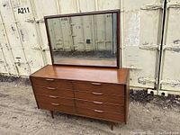 Full view of dresser and mirror outdoors against metal containers