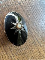 Front of black oval mourning brooch with central pearl and rhinestone star accent on wooden surface