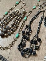 Photo of various necklaces including silver-tone bead strands, gold-tone chain with turquoise-like beads, and black beaded necklaces.