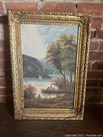 Full view of oil painting showing lake scene with sailboats, trees, and distant mountains in an ornate gilt frame.