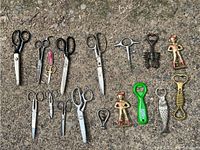 Full view of all scissors and bottle openers laid out on rough surface showing variety of sizes and styles.