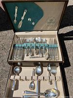 Full view of silverware set arranged inside original box showing forks, knives, spoons, serving pieces, and box interior structure and lining.