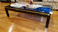 Front angled view of the black lacquer coffee table showing its rectangular shape, glass top, and finished legs. Some scratches are visible on the lacquer surface.
