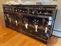 Full front view of sideboard showing three drawers, four doors, brass hardware, mother-of-pearl figures and glass top