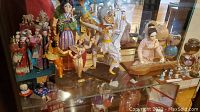 Display of various Asian dolls including wooden Chinese dolls, Thai dancers, and miniature figurines in a glass cabinet.