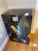 Front angled view showing the lacquer cabinet with floral and bird designs and multiple drawers with keyhole locks.