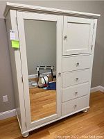 Frontal view of white armoire showing mirrored left door and right drawers