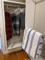 White and blue striped quilted bedspread hanging on closet door with two plaid wool blankets hanging inside closet.
