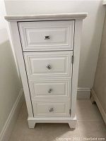 Front view of white cabinet showing one drawer on top and door below with three visible square knobs
