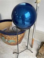 Blue reflective garden ball resting on black metal stand with curled top supports and tripod base.