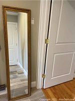 Full view of the cheval mirror showing entire length and gold-tone carved frame around reflective glass.