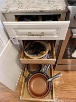 Open drawers showing assortment of cooking utensils, baking tools, dough bowl, and non-stick skillets with copper interiors.