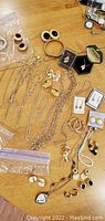 Overview of assorted gold-tone costume jewelry laid out on table, showing chains, earrings including clip-on styles, pendants, and bead strands.