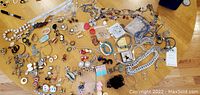 Wide view of assorted costume jewelry laid out on table showing rings, earrings, pins, beads, necklaces, and chains.
