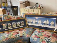Two framed prints on floral couches, showing Lighthouses of Cape Cod and Salecraft sailboats, both matted in navy blue with gold frames.