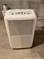 Front view of the white Comfort-Aire dehumidifier in a basement setting, showing vented front panel and control panel top.