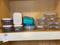 Wide shot of all food storage containers arranged on a wooden shelf showing clear glass containers, blue and turquoise plastic containers, and several press-seal plastic containers with white lids.