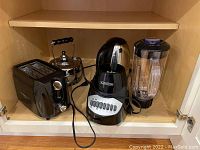 Shelf with a Bella toaster, Black & Decker blender, and Aroma electric water kettle, all black appliances