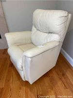 Front angle view showing padded backrest and armrest with cream leather-like material on wooden floor.