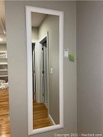 Full front view of the rectangular full-length mirror with white frame hanging on the wall showing its size and style