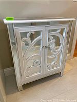 Mirrored cabinet showing white scroll facade on front doors with mirrored sides and top