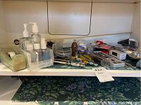 Shelf with hand sanitizer bottles, glass beaded handle letter openers, tape dispenser, small tools, and other office supplies arranged together.