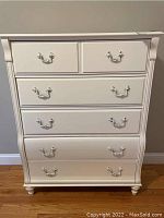 Front view of white five-drawer dresser with silver bail handles and turned feet